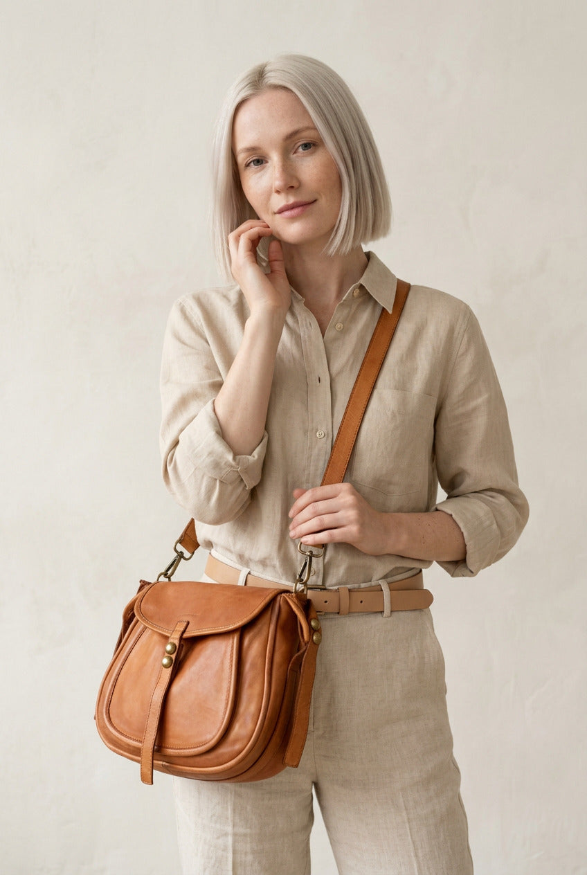 Une femme porte un sac à main en cuir sur l'épaule. Le sac bandoulière est de couleur cognac.