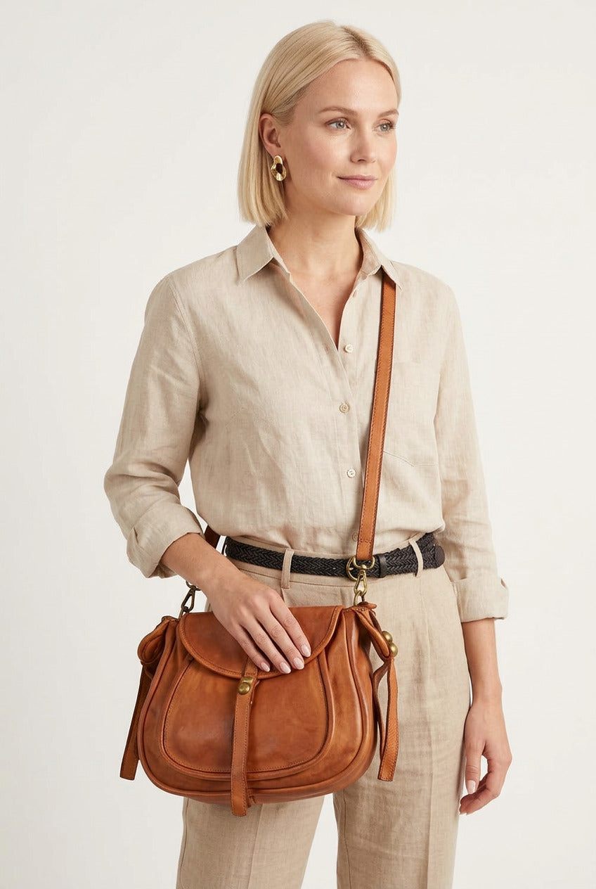 Une jeune femme vêtue de beige porte un sac à main en cuir en bandoulière. Le sac à main est en cuir italien de couleur cognac.
