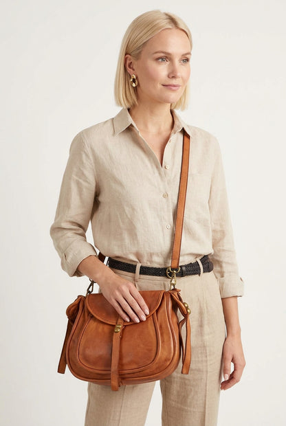 Une jeune femme vêtue de beige porte un sac à main en cuir en bandoulière. Le sac à main est en cuir italien de couleur cognac.