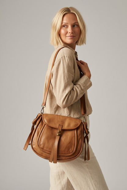 Femme en tenue beige portant un sac bandoulière pour femme en cuir couleur cognac de style bohème