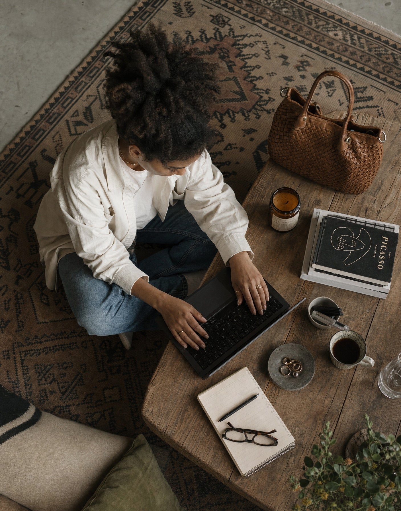 Elegante Frau im urbanen Outfit platziert ihren großen geflochtenen Leder Shopper in cognac-braun auf einem Tisch im Außenbereich eines europäischen Cafés