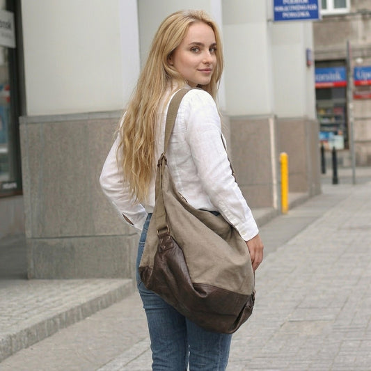 Blonde Frau in weißer Leinenbluse und blauen Jeans steht auf einer städtischen Straße und trägt die khakibraune Canvas Hobo-Tasche lässig über der Schulter. Lifestyle-Produktfotografie im urbanen Stil