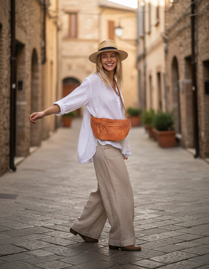Rückansicht: Frau blickt auf historische italienische Architektur, lässig getragene XXL Leder Bauchtasche in Cognac zum sommerlichen Look